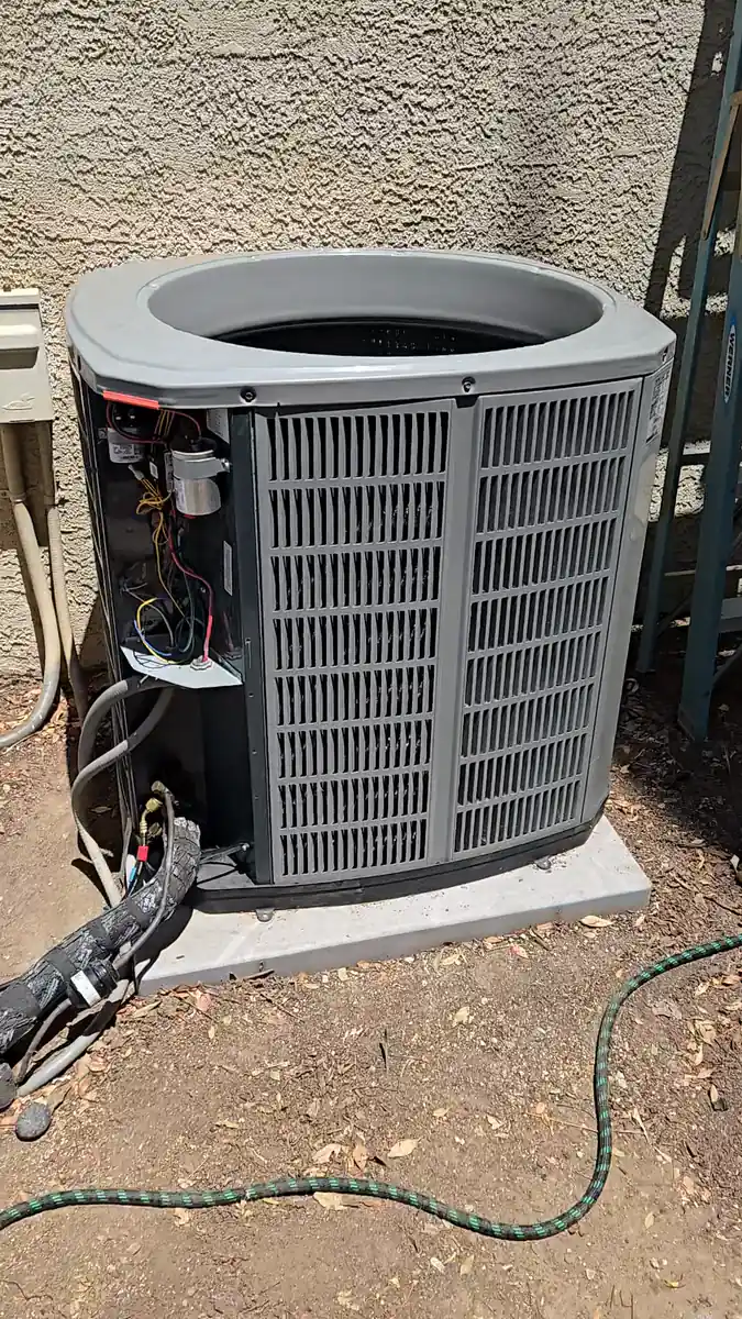 Una unidad condensadora de exterior con la rejilla superior del ventilador quitada y el panel lateral de servicio abierto durante el cambio de compresor