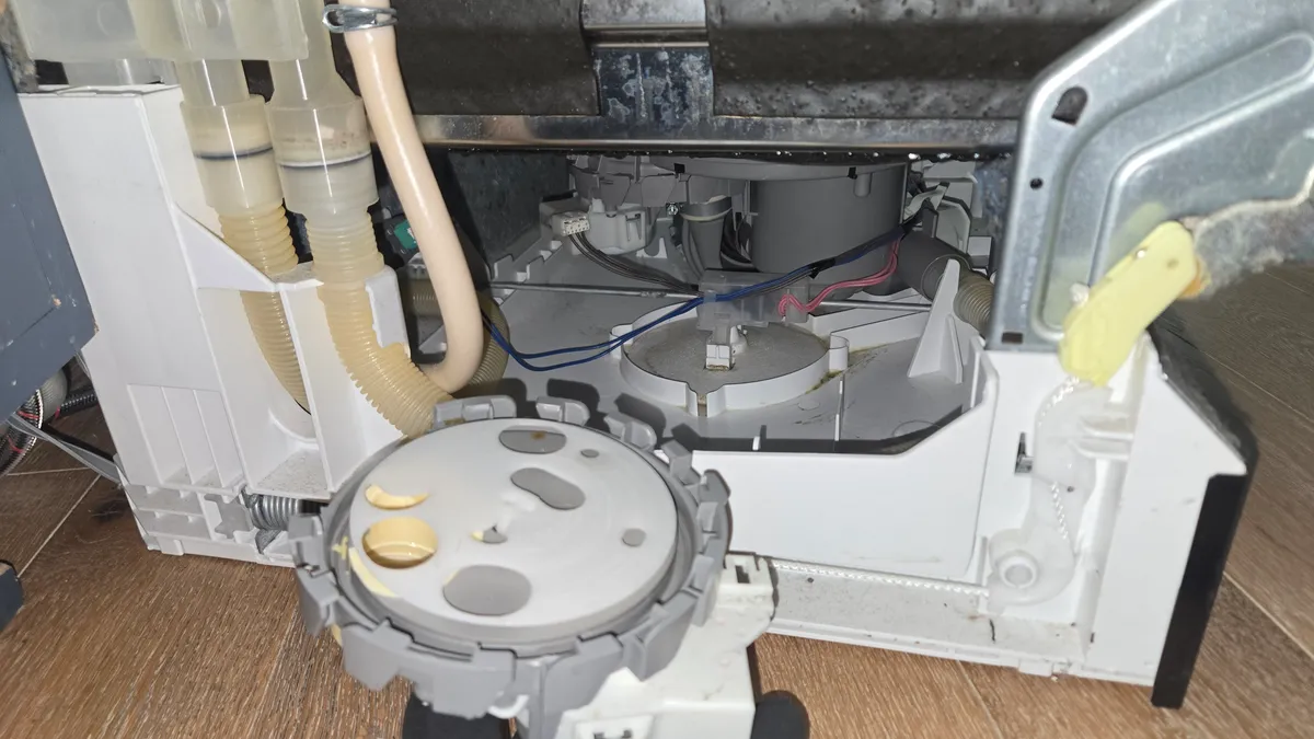 Base de un lavaplatos Bosch abierta por debajo, con el conjunto redondo del desviador en una mano con guante