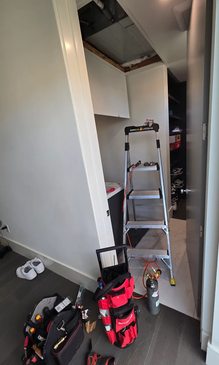 Panel de acceso abierto en el techo de un clóset del pasillo, con una escalera de tijera abajo, en una manejadora de mini-split oculta en un condominio de Hollywood