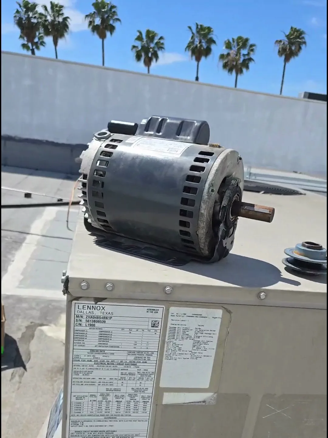 Un técnico reemplazando un motor de ventilador quemado dentro de una unidad paquete de techo comercial que da servicio a un salón de uñas en Los Ángeles.