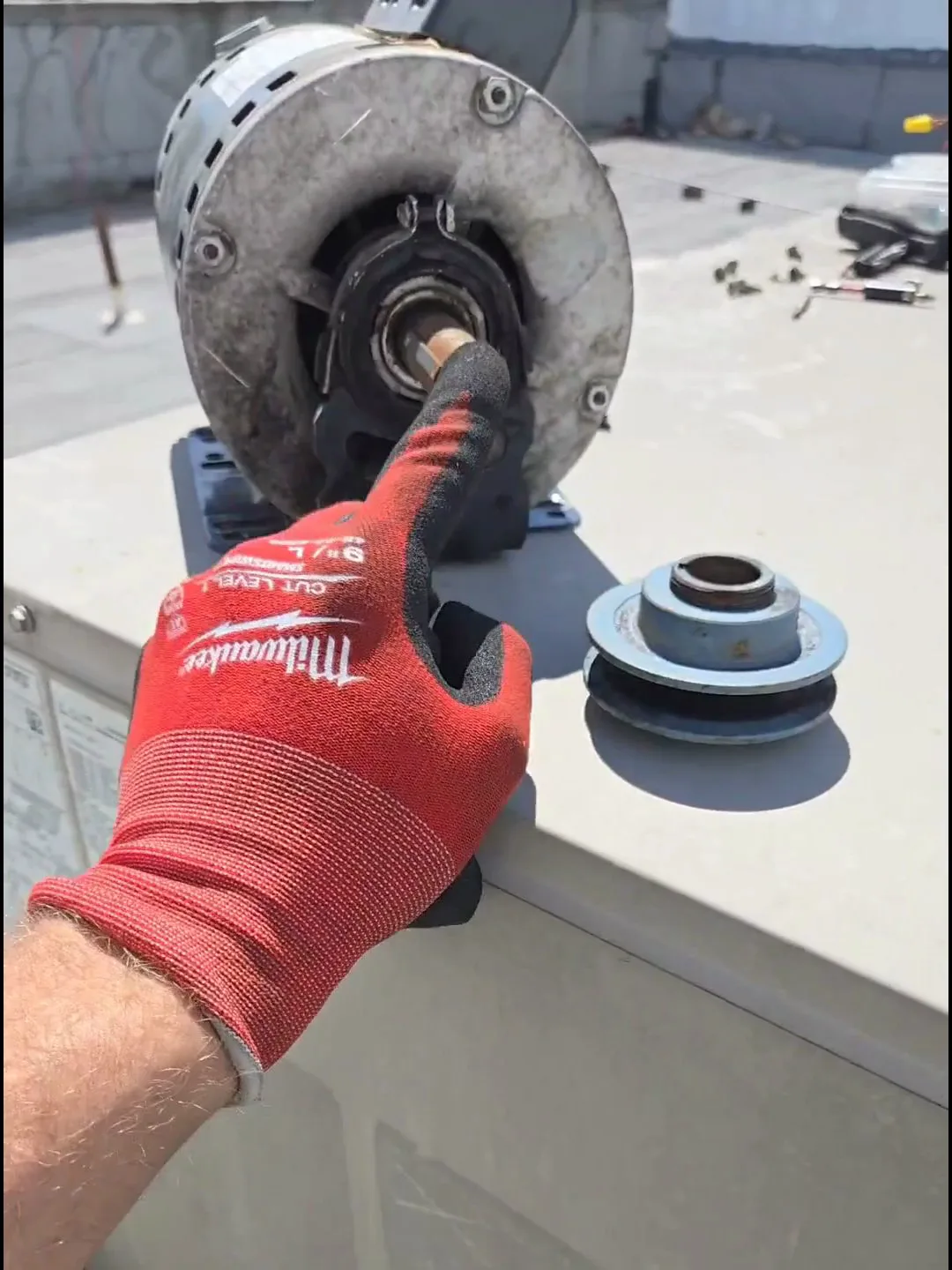 El eje de 5/8" del motor nuevo junto a la polea vieja, cuyo barreno más grande no encajaba — el desajuste que obligó a ir a la casa de repuestos.