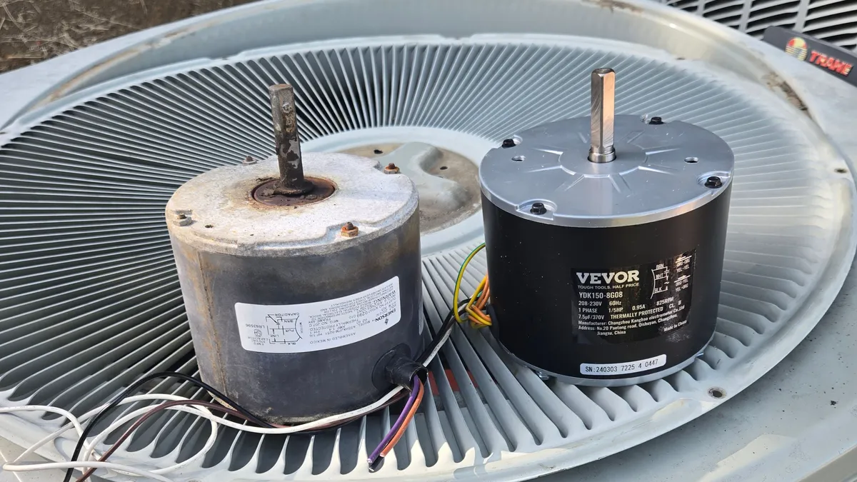 The old condenser fan motor with a rusted shaft next to a new black replacement motor, both resting on the fan grille on top of an AC condenser