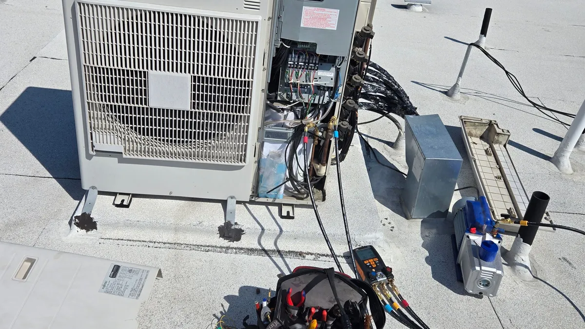 Unidad exterior multizona Fujitsu en una azotea plana, con el lado de servicio abierto, un manojo de líneas de refrigerante aisladas y mangueras de manómetro conectadas