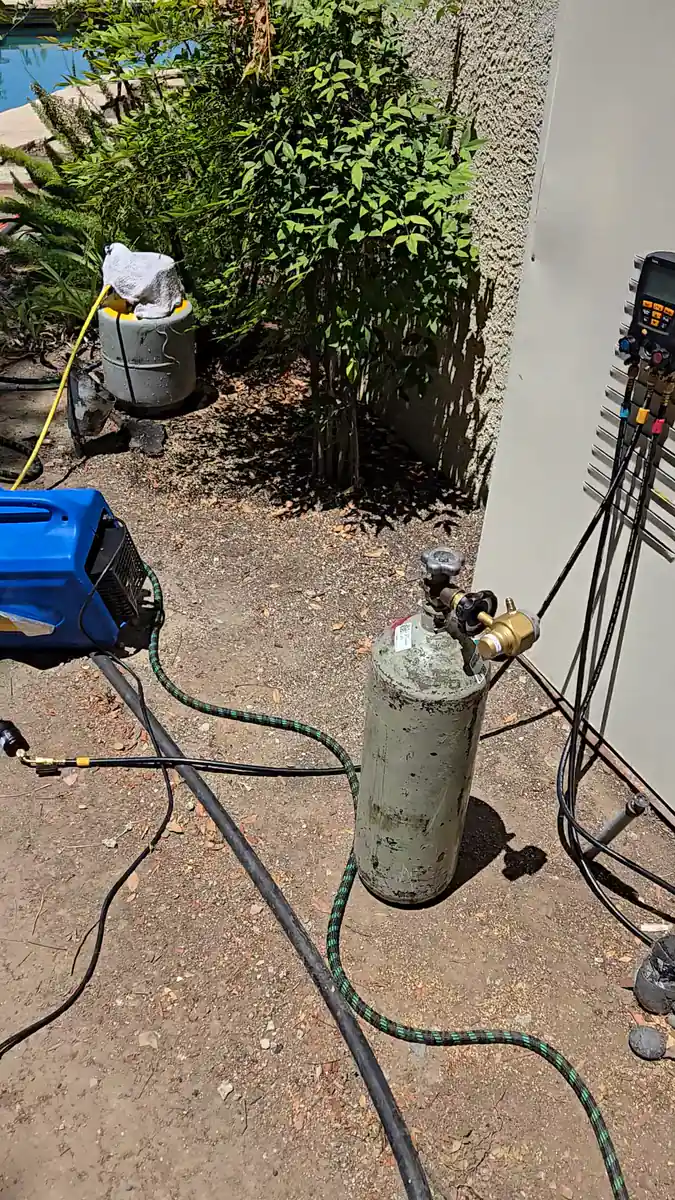 Un cilindro de nitrógeno con su regulador, manómetros digitales colgados en la pared y un cilindro de refrigerante con manguera amarilla, montados al lado de la unidad