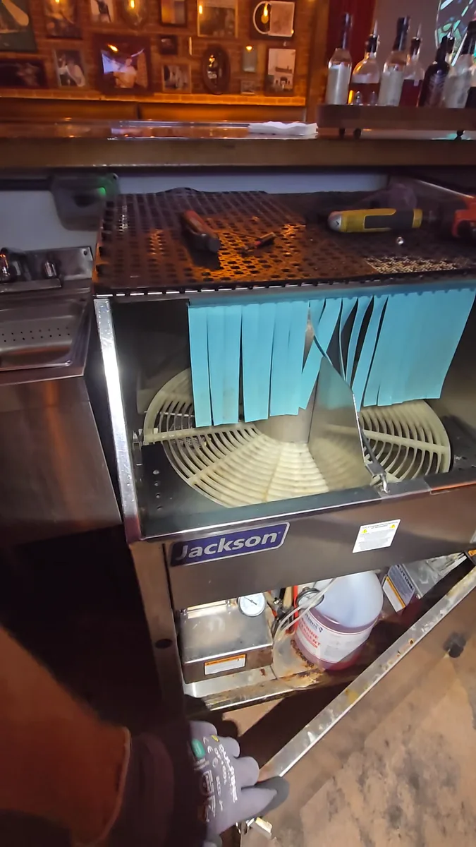 Jackson carousel glasswasher built in under a bar counter with its top open, showing the rack that had stopped turning