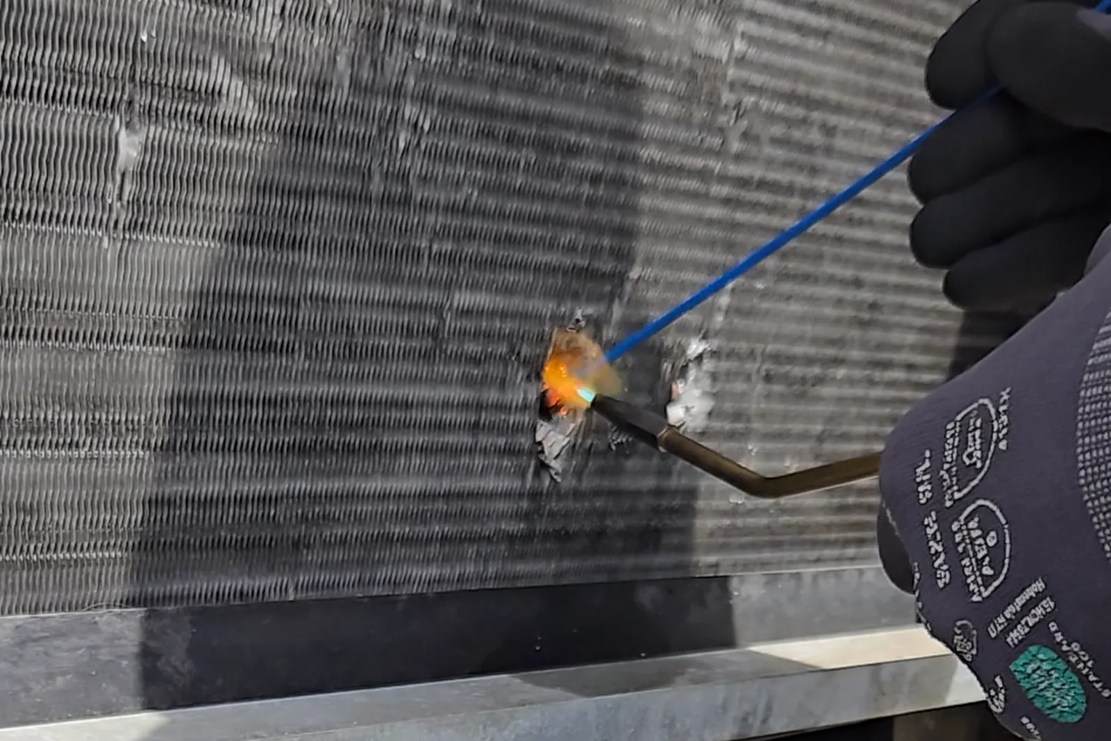 Brazing torch sealing a punctured copper evaporator tube on a rooftop Lennox package unit