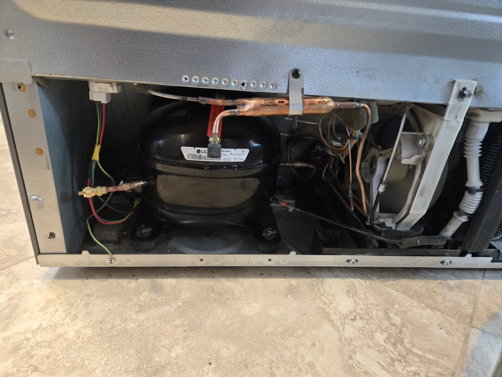 El compresor R134a de repuesto instalado en un refrigerador LG LFX25991ST, con una válvula perforadora roja en la línea durante una reparación de sistema sellado en Los Ángeles.