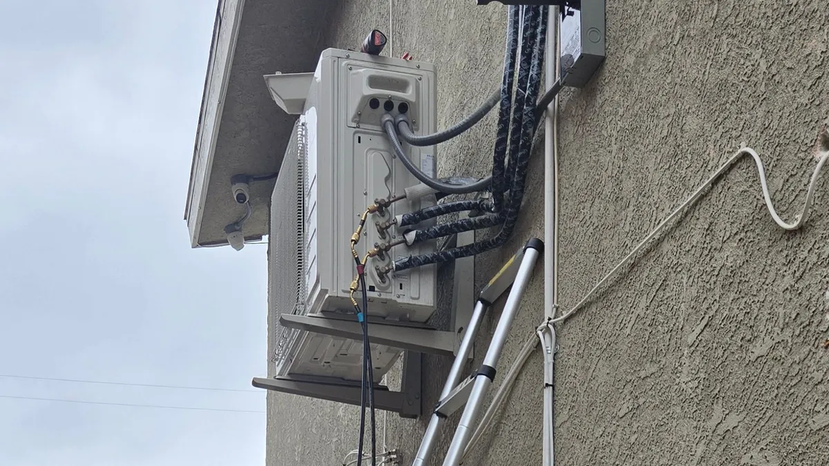 Mini-split outdoor unit on a wall bracket under the eave, with insulated line sets leaving its side and service hoses connected