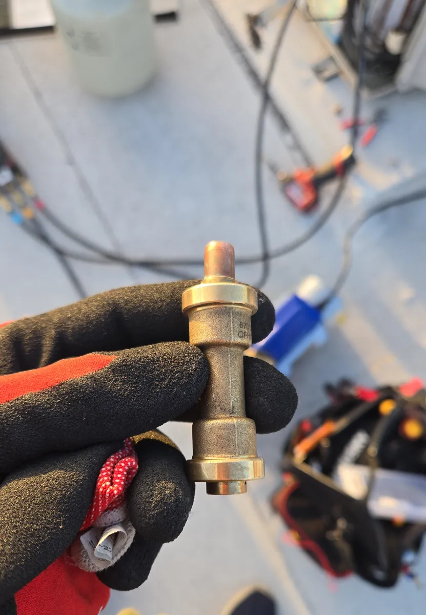El acople rápido de refrigerante cortado de un mini-split ducteado en un condominio de Hollywood, sostenido en una mano con guante