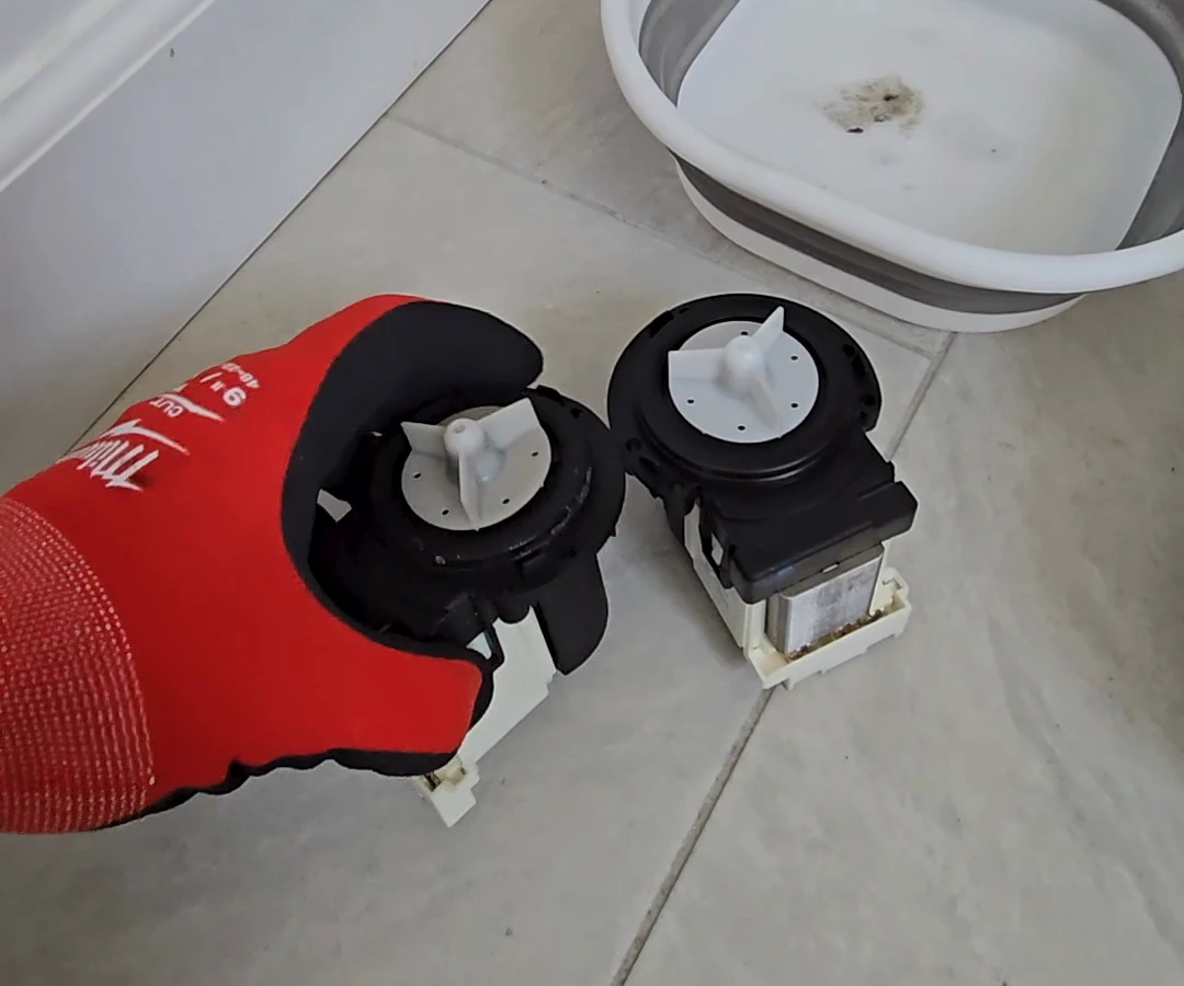 Removed LG drain pump held in a red glove beside the replacement pump