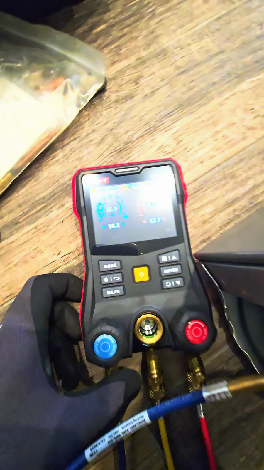 Digital manifold gauge held in a gloved hand, low-side reading about 15 PSI on a refrigerator that is not cooling