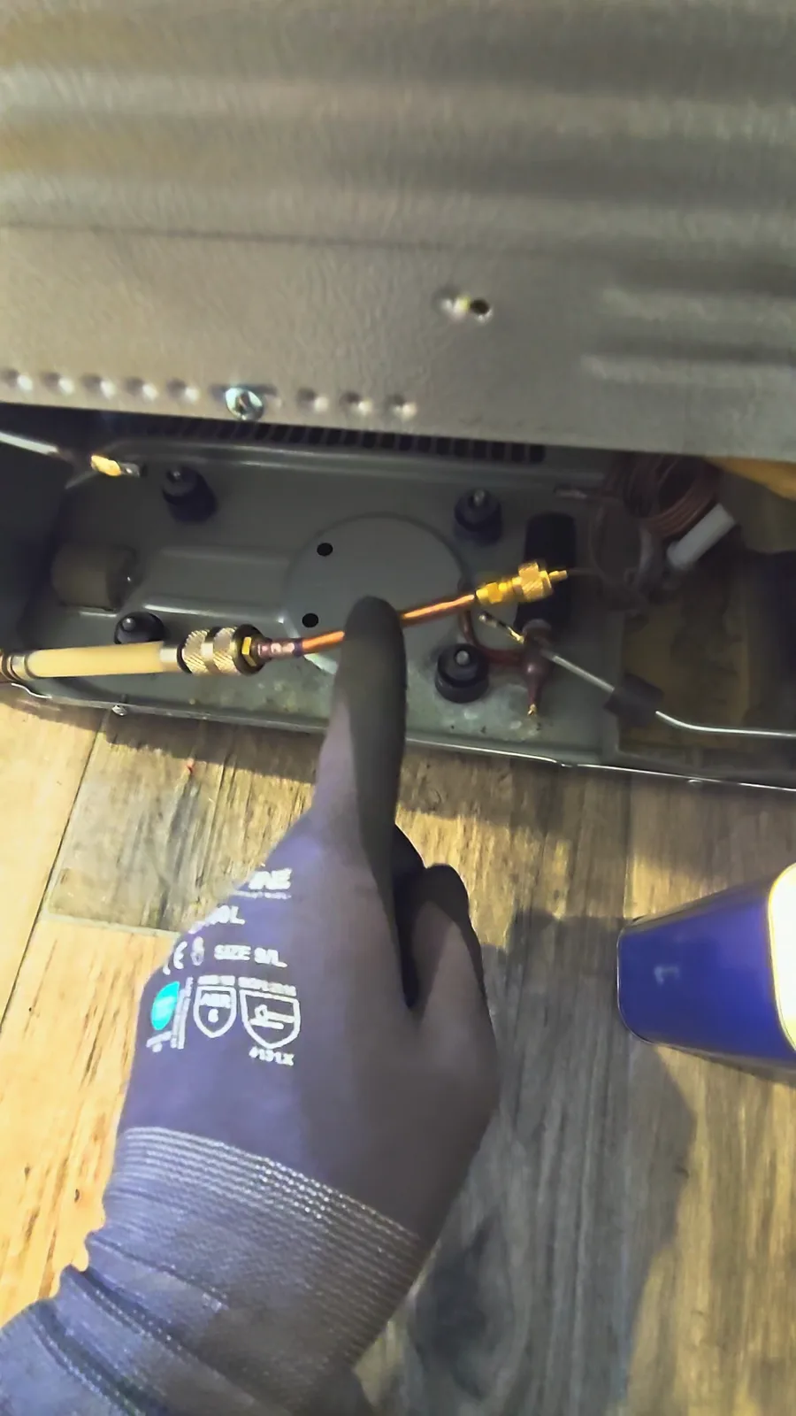 Gloved finger pointing at a homemade adapter connected to the capillary tube at the back of the refrigerator for a nitrogen flush