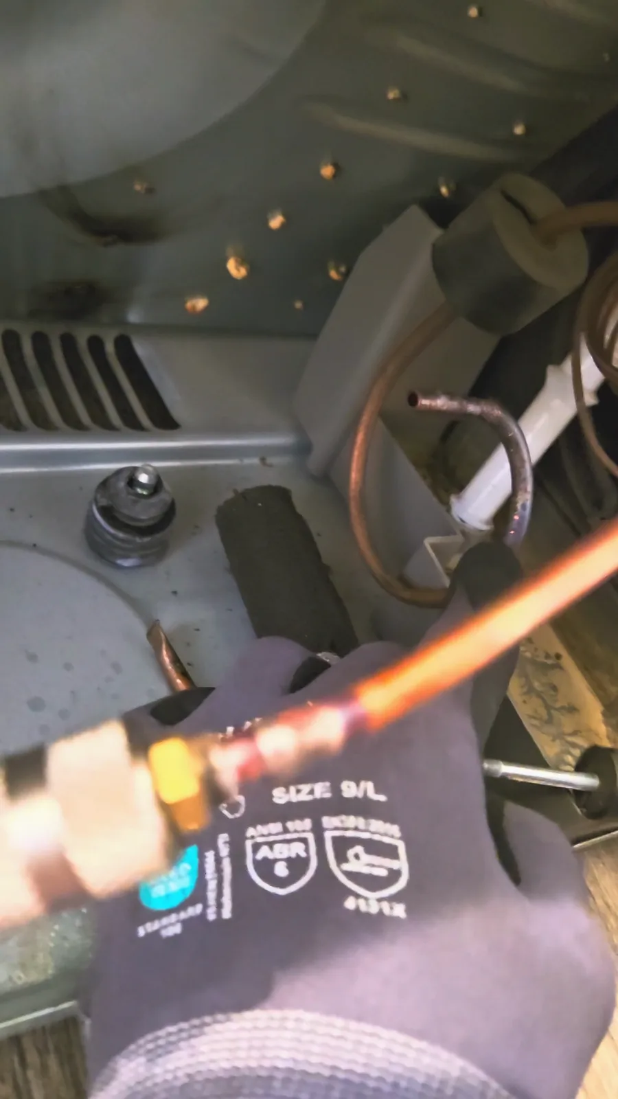 Gloved hand holding a copper line with a fitting connected during the high-pressure nitrogen flush of the refrigerant circuit