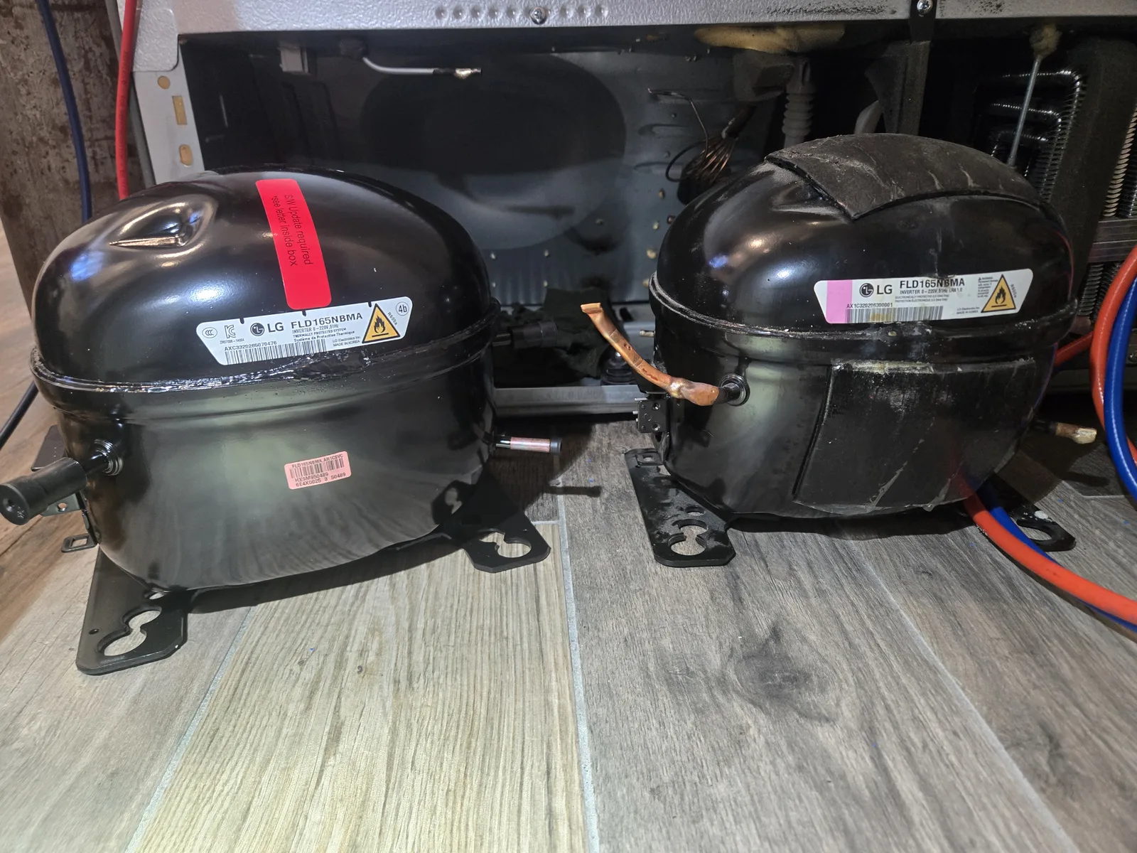 Old and new LG compressors side by side on the floor, the new one with a red firmware-update tag