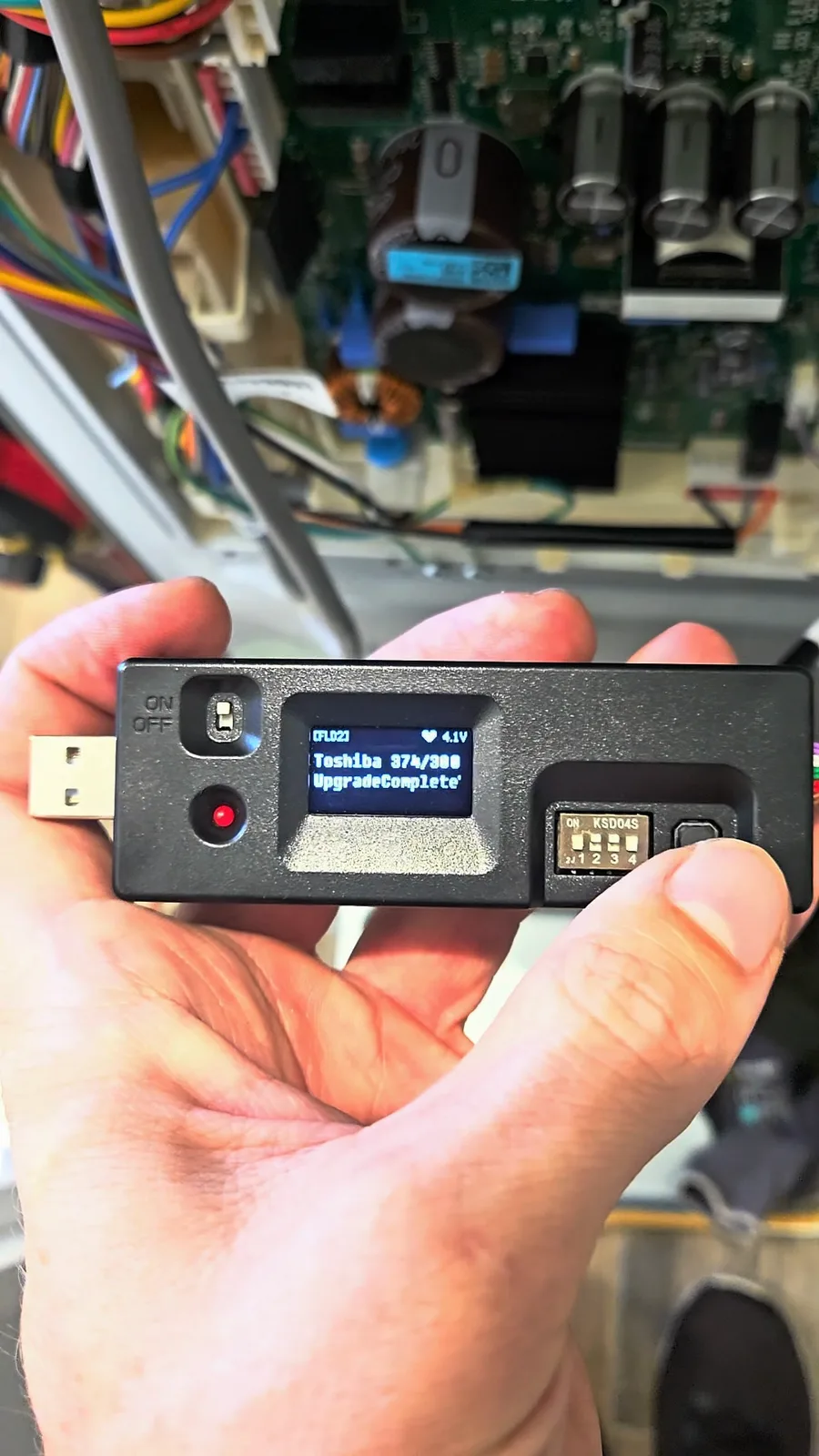 Handheld programmer connected to the refrigerator control board, its screen showing the firmware upgrade as complete