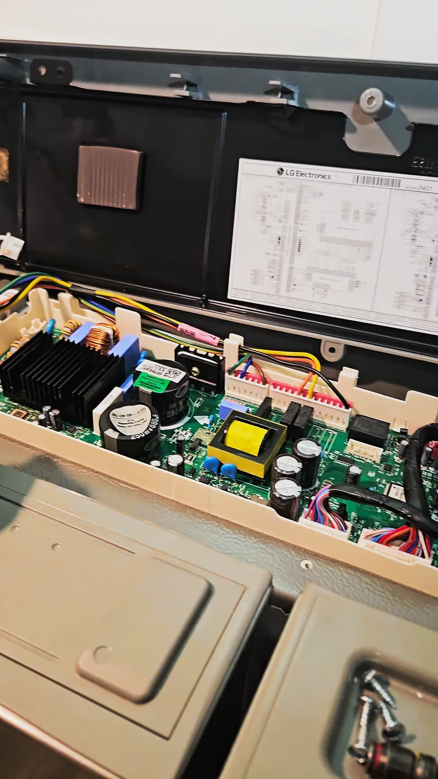 Open control panel at the top of the refrigerator with the circuit board and the wiring diagram sheet inside