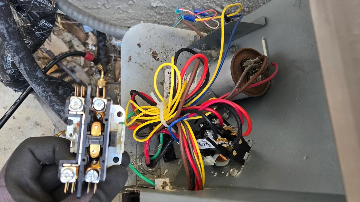 Burnt contactor held in a gloved hand beside the open electrical compartment of a York AC condenser