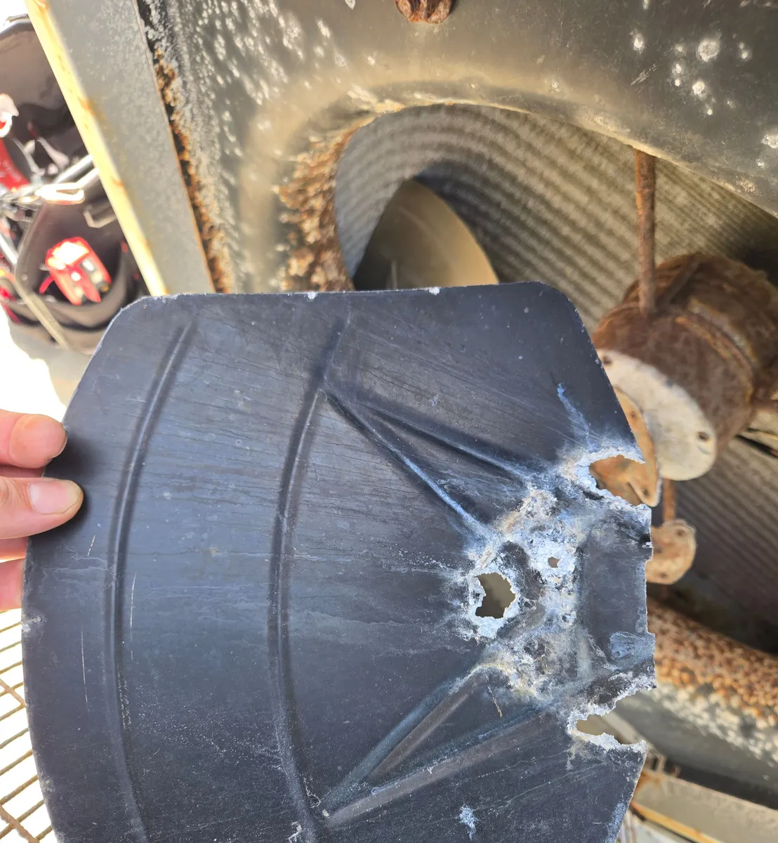 A detached condenser fan blade held in hand, its mounting area corroded into holes with white powdery deposits, with the rusted fan motor behind it