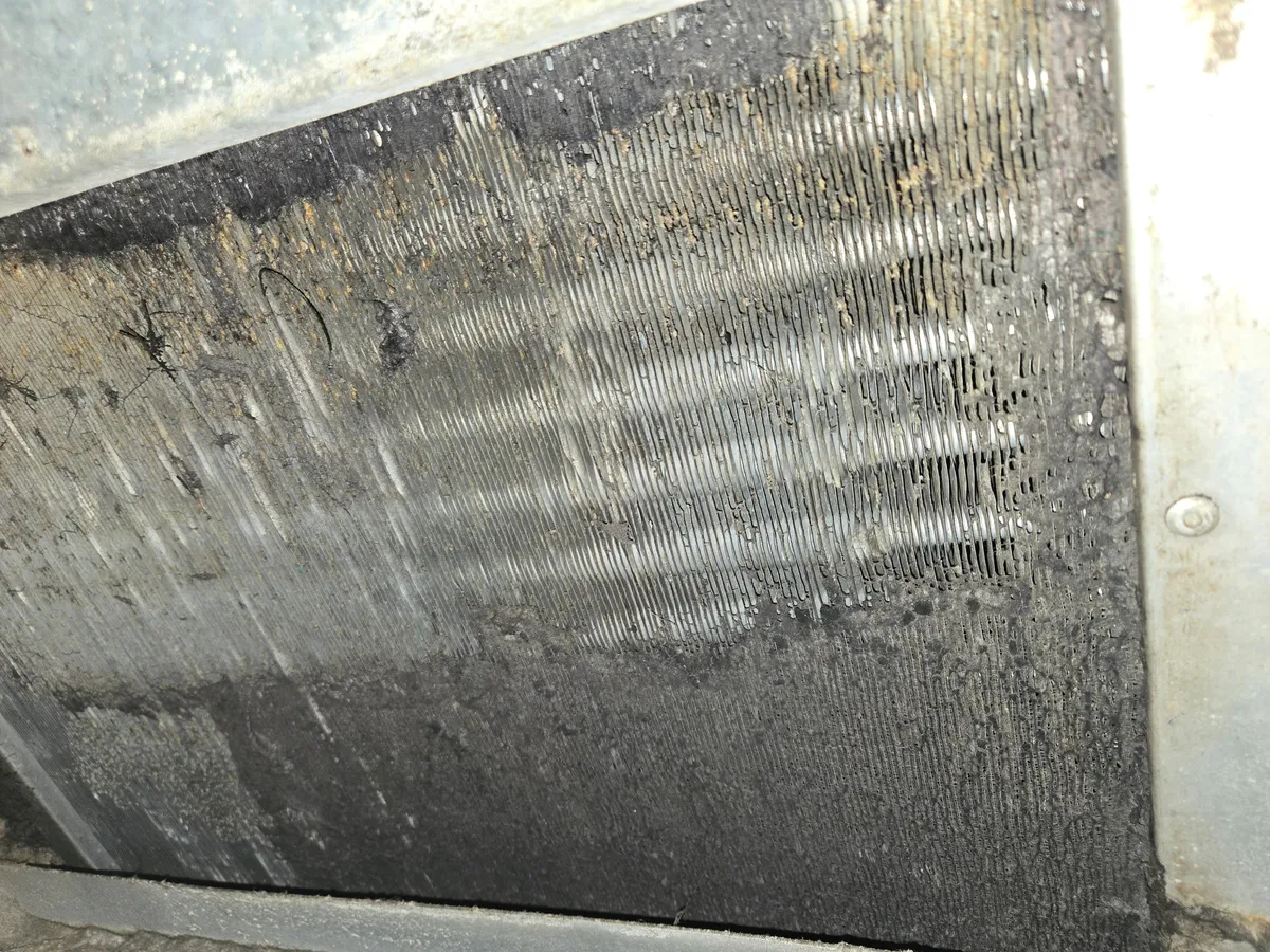 Face of an evaporator coil partway through cleaning: a brushed strip of bare fins in the middle, with a dark mat of dust still covering the rest