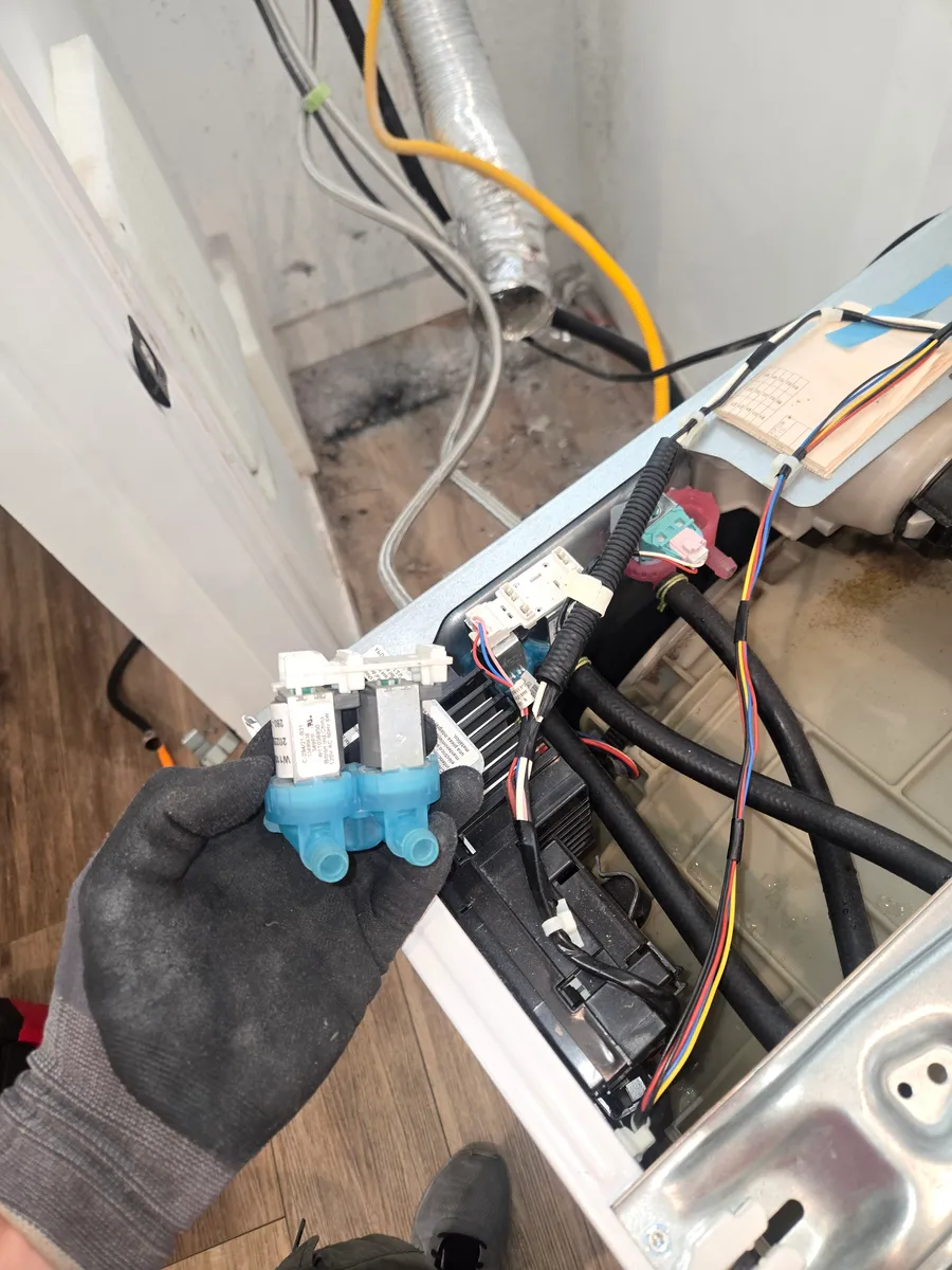 Water inlet valve held beside an opened Maytag washer during service